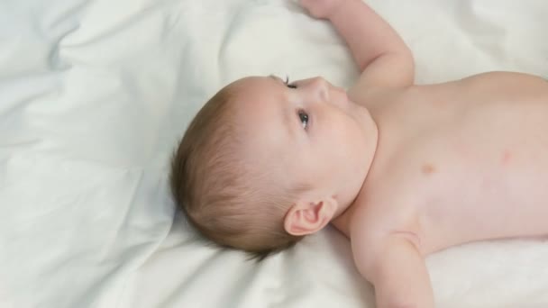 Портрет красивого смешного новорожденного малыша двух месяцев, лежащего на белой кровати — стоковое видео