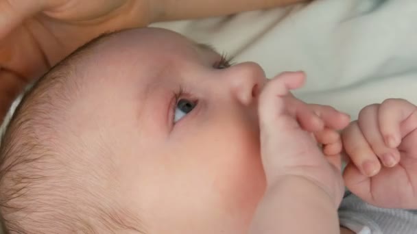 Mother gently touches and cradles her newborn baby in arms while sitting on her bed. The childs face close up view — Stock Video