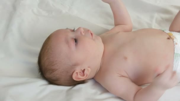 Portret pięknego śmiesznego małego noworodka z dwóch miesięcy leżącego na białym łóżku. Mama ubiera dziecko — Wideo stockowe