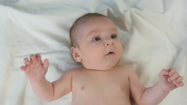 Portret van mooie grappige kleine pasgeboren baby van twee maanden liggend op wit bed — Stockvideo