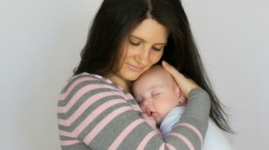 Uzun koyu saçlı genç güzel anne stüdyoda beyaz arka plan üzerinde iki aylık yeni doğmuş bir bebek bebek tutuyor