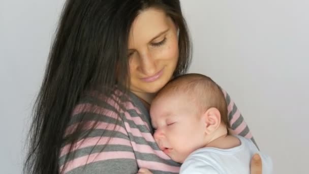 Young beautiful mother with long dark hair is holding a newborn infant baby of two months on white background in studio — Stock Video