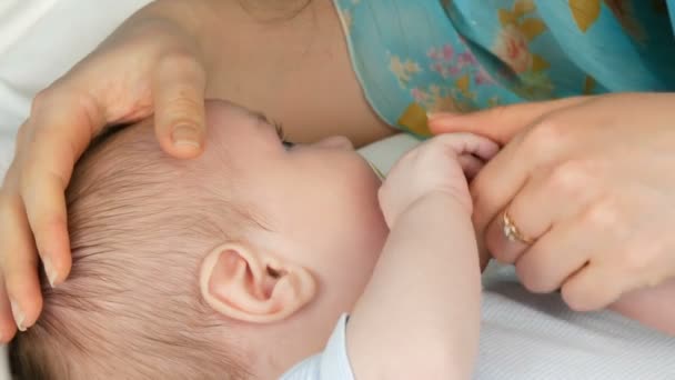 Mother gently touches and cradles her newborn baby in arms while sitting on her bed. The childs face close up view — Stock Video