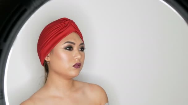 Krásná Korejská Asijská dívka v módním červeném turbanu s jasným večerem make-up zakouřené oči, které pózující ve studiu na bílém pozadí — Stock video