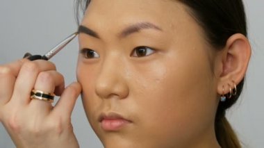 Profesyonel makyaj sanatçısı özel fırça ile Asyalı Koreli kadın modelin yüzüne kaşboyaları.