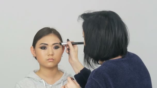 Artista de maquillaje profesional aplica corrector de fundación o resaltador a la cara de modelos coreanos asiáticos con cepillo especial — Vídeos de Stock