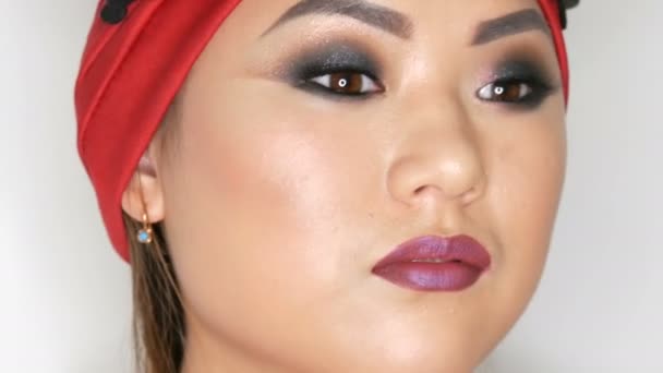 Gyönyörű koreai ázsiai lány egy trendi vörös turbán fényes esti make-up füstös szeme pózol stúdióban fehér alapon — Stock videók