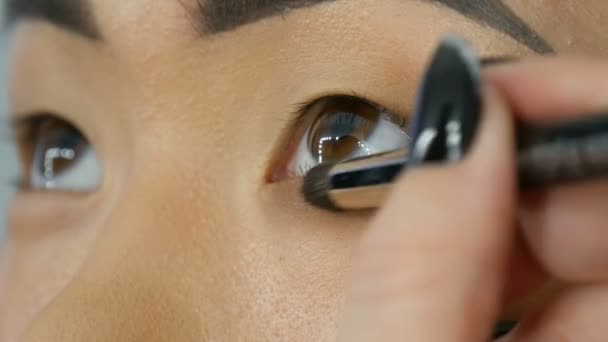 Profesional maquillaje artista hace maquillaje de ojos de chica coreana mujer asiática con cepillo especial — Vídeos de Stock