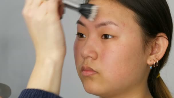 Profesyonel makyaj sanatçısı özel fırça ile Asya Koreli modeller yüz vakıf kapatıcı veya vurgulayıcı uygular — Stok video