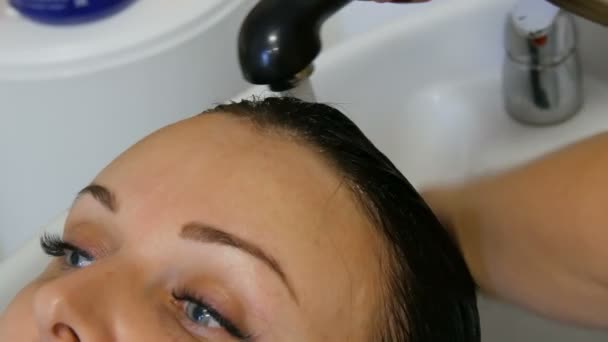 Mujer en un salón de belleza o peluquería lavar su cabello en un fregadero especial. Concepto de peluquería en el trabajo. Hermosa mujer con ojos azules y pestañas extendidas — Vídeos de Stock