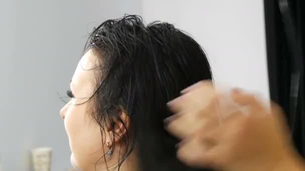 Mulher bonita está secando seu longo cabelo preto com um secador de cabelo no salão de beleza ou cabeleireiro — Vídeo de Stock