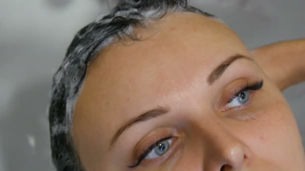 Женщина в салоне красоты или парикмахерской моет волосы в специальной раковине. Концепция парикмахерской на работе. Красивая женщина с голубыми глазами и длинными ресницами — стоковое видео