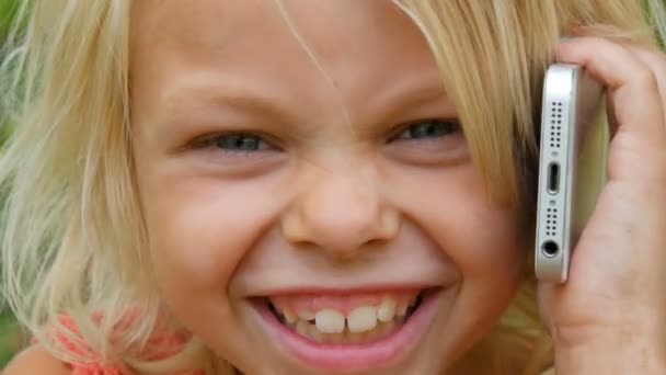Retrato de una linda rubia de ojos azules niña de siete años con la cara sucia riendo mientras habla en un teléfono móvil — Vídeos de Stock