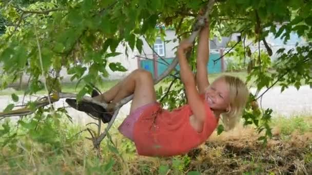 Zeven jaar grappig vies kind meisje blonde hangt op een boomtak buiten de stad op de zomerdag — Stockvideo