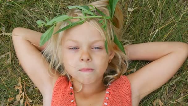 Aranyos kék szemű szőke hét éves lány egy piszkos arcát. Gyermek feküdt a fűben a kezét a feje mögé rágás száraz szalma. — Stock videók