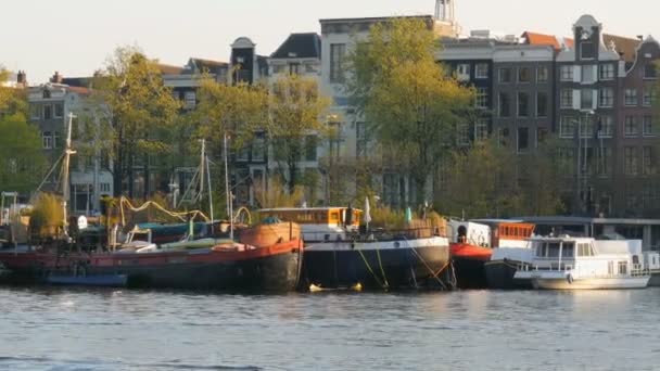 Amsterdã, Holanda - 21 de abril de 2019: Turistas navegam de barco ao longo do canal de Amsterdã, no qual ancoram barcos. Autênticas casas e ruas holandesas da capital dos Países Baixos — Vídeo de Stock