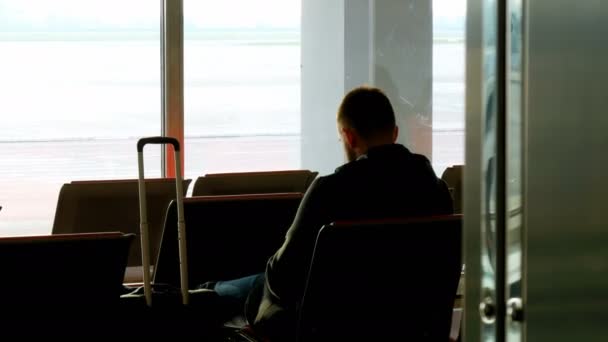 Силуэт мужчины с чемоданом, ожидающего в аэропорту перед отъездом — стоковое видео