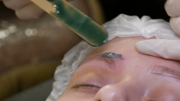 Epilation des sourcils. Une cire verte spéciale est appliquée sur la peau pour éliminer l'excès de poils et façonner les sourcils . — Video
