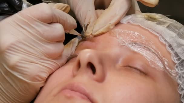 Ett ögonbryn under narkos. På den andra mästaren applicerar kosmetologen pigment för att färga ögonbrynen. Korrigering av ögonbrynsform med microblading. Tatuering, permanent makeup, pulversprutning — Stockvideo