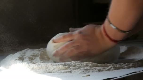 Las manos femeninas amasan la masa en la cocina vintage de la casa en el pueblo. Un rayo de sol cae sobre la masa y la harina volando en el aire. Hornear en casa — Vídeo de stock