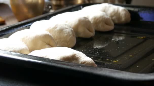 Vrouw handen bakker legt zelfgebakken deeg in de vorm van langwerpige ronde ballen in rij op zwart bakplaat klaar om te koken in de oven, close-up uitzicht home dorp keuken — Stockvideo
