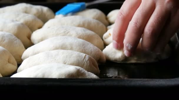 Vrouw handen bakker zet deeg in de vorm van langwerpige ronde ballen op een rij op zwarte bakplaat, close-up uitzicht zelfgemaakt gebak, dorp keuken — Stockvideo