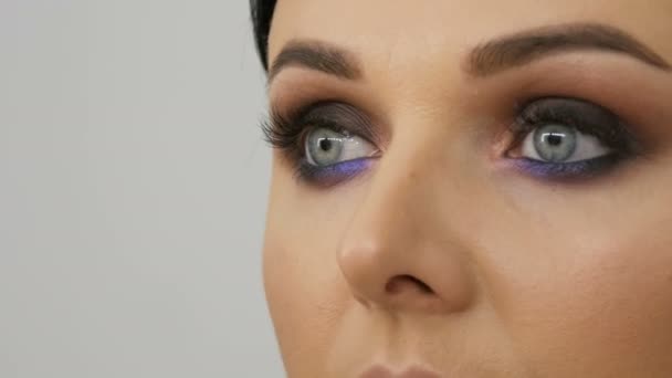 Makeup artist gör modeller sotade ögon med hjälp av speciell borste Lilac och pärlskimrande sotade ögon ögonskugga, ögon och ansikte kvinna närbild. Professionellt mode. — Stockvideo