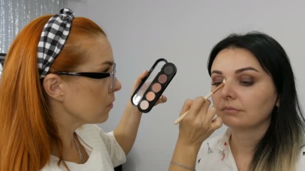 Palet met verschillende tinten beige in de handen van een make-up kunstenaar die professionele make-up doet. Mooie avond make-up wordt toegepast op een jonge vrouw — Stockvideo