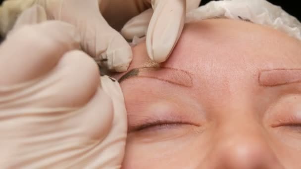 Die Hände einer Kosmetikerin in weißen Handschuhen tragen mit Hilfe eines speziellen Stifts Pigment auf die Haut auf. Augenbrauenkorrektur. Microblading, Permanent Make-up, Permanent Make-up, Pudersprühen — Stockvideo