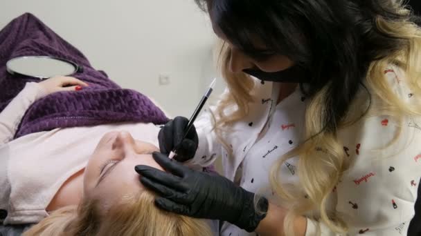 Schoonheidsspecialiste verandert wenkbrauw vorm correctie voor cliënt die op de bank ligt. Microblading, tatoeage, permanente make-up. Cosmetologie procedure in schoonheidskliniek. — Stockvideo