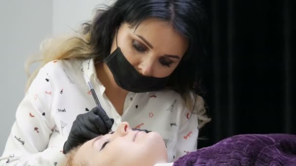 Mooie vrouw stylist make-up kunstenaar schoonheidsspecialiste maakt wenkbrauw correctie op het gezicht van een patiënt die op een speciale bank in beauty studio ligt — Stockvideo