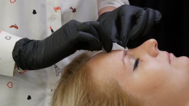 L'esthéticienne corrige les sourcils de son patient. Dégraisser la peau avant la procédure avec une lingette alcoolisée spéciale — Video