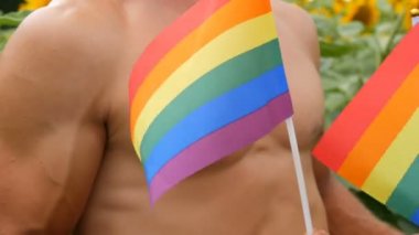 Atletik kaslı genç bir erkek elinde gökkuşağı taşır Neşeli gurur sembolü Lgbt bayrağı alışılmadık oryantasyonun, yazın açan ayçiçeklerine karşı