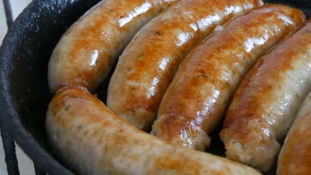 Thick fatty delicious fresh sausages are fried in a pan in the home kitchen. Fried meat products making sausages for beer. White Munich or Bavarian sausages close up view — Stock Video