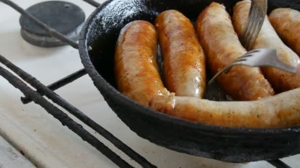 Παχιά λιπαρά νόστιμα φρέσκα λουκάνικα τηγανίζονται σε ένα τηγάνι στην κουζίνα του σπιτιού. Τηγανητά προϊόντα κρέατος που φτιάχνουν λουκάνικα για μπύρα. Πιρούνι μετατρέπει Fried Λουκάνικα — Αρχείο Βίντεο
