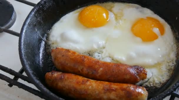 在平底锅里吃着有趣的早餐，面带微笑，眼神带笑。两个煎蛋和浓密的巴伐利亚香肠，用老式铁锅在煤气炉上煎 — 图库视频影像