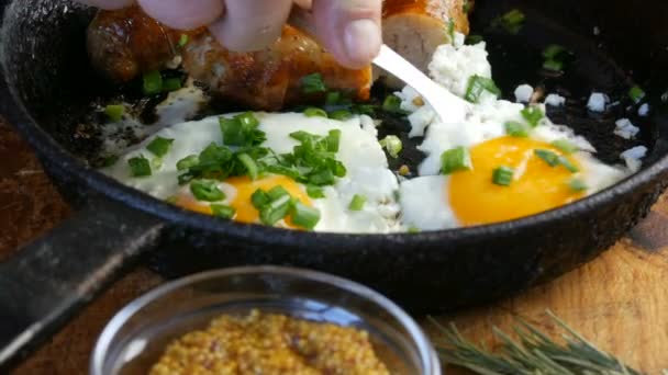 Un hombre come huevos fritos en una sartén antigua con salchichas tostadas blancas bávaras y cebollas verdes frescas, junto a la mostaza francesa. Estilo rústico de servir comida — Vídeo de stock