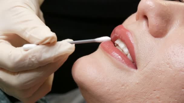 Schoonheidsspecialiste raakt een wattenstaafje aan voor permanente tattoo lip make-up. Lichte matte roze lippen dicht. Procedure voor het microbladen van lippen. — Stockvideo