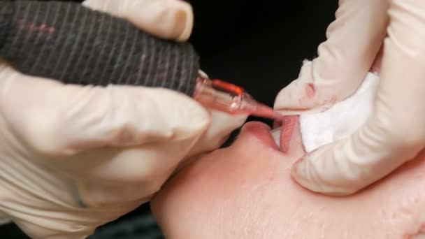 Microblading τατουάζ χειλιών με ειδικό χρωματισμό κόκκινη χρωστική ουσία που διορθώνει το χρώμα των χειλιών στην κλινική κοσμετολογίας. Μόνιμη διαδικασία μακιγιάζ χείλη εφαρμογή χρωστική μακιγιάζ στα χείλη με ένα μηχάνημα τατουάζ κοντά — Αρχείο Βίντεο
