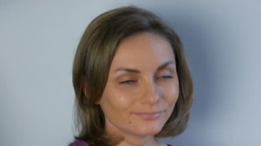 Genç ve güzel bir kadının portresi. Kadın saçına dokunur, düşünceli bir şekilde kameraya bakar ve nazikçe gülümser.