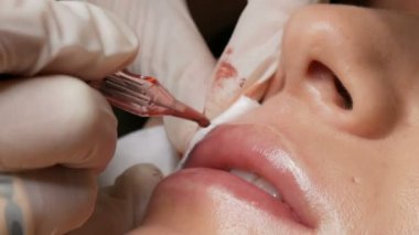 Kozmetik uzmanı, dövme makinesi pembe pigmenti kullanarak dudaklarını mikro patinaj yaptırıyor. Kadın dudaklarına pigment makyajı yapan bir güzellik uzmanı. Güzellik salonunda güzellik endüstrisi kavramı