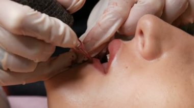 Kozmetik uzmanı, dövme makinesi pembe pigmenti kullanarak dudaklarını mikro patinaj yaptırıyor. Kadın dudaklarına pigment makyajı yapan bir güzellik uzmanı. Güzellik salonunda güzellik endüstrisi kavramı