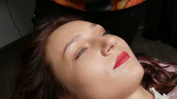 Porträt einer schönen jungen Frau vor permanentem Make-up durch Microblading mit Augenbrauen-Tätowierung und Lippen mit rotem Lippenstift liegt auf einer Couch in einem Schönheitssalon — Stockvideo