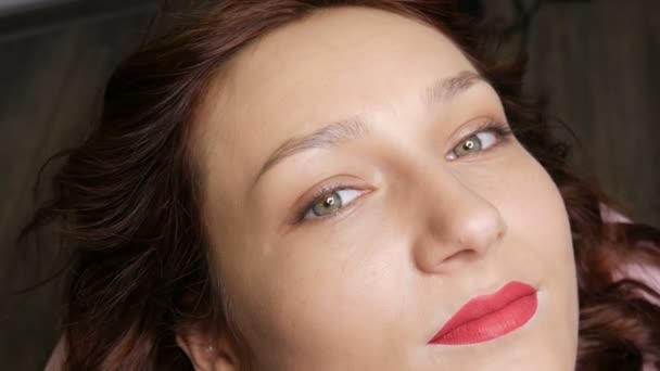 Portrait d'une belle jeune femme avant maquillage permanent par microblading avec tatouage de sourcil et lèvres avec rouge à lèvres repose sur un canapé dans un salon de beauté — Video