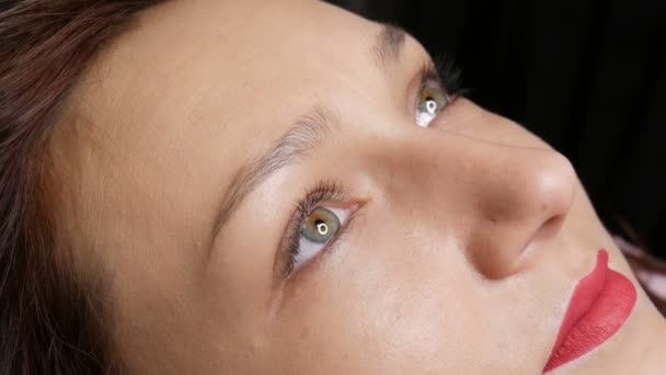 Porträtt av en vacker ung kvinna innan permanent makeup genom microblading med ögonbrynstatuering och läppar med rött läppstift ligger på en soffa i en skönhetssalong — Stockvideo