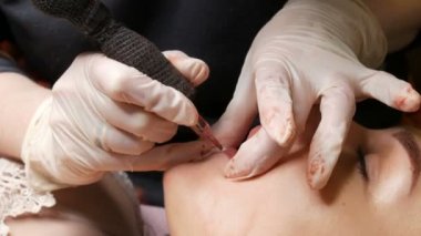 Kozmetik uzmanı, dövme makinesi pembe pigmenti kullanarak dudaklarını mikro patinaj yaptırıyor. Kadın dudaklarına pigment makyajı yapan bir güzellik uzmanı. Güzellik salonunda güzellik endüstrisi kavramı