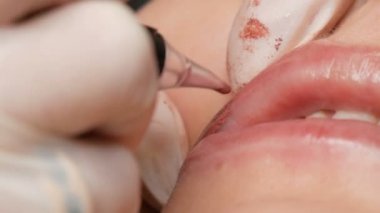 Kozmetik uzmanı, dövme makinesi pembe pigmenti kullanarak dudaklarını mikro patinaj yaptırıyor. Kadın dudaklarına pigment makyajı yapan bir güzellik uzmanı. Güzellik salonunda güzellik endüstrisi kavramı