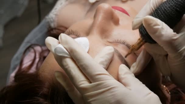 Vackrare i svarta handskar gör permanent makeup korrigering av formen på ögonbrynen till en ung vacker flicka. Mikroblads, ögonbrynstatuering i skönhetssalong — Stockvideo