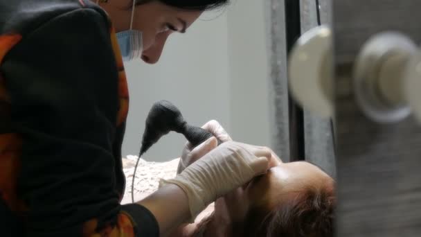 Cosmetologist mãos fazendo lábios microblading procedimento permanente usando pigmento rosa máquina de tatuagem. Esteticista aplicando maquiagem pigmento em lábios de mulher. Conceito da indústria da beleza no salão de beleza — Vídeo de Stock