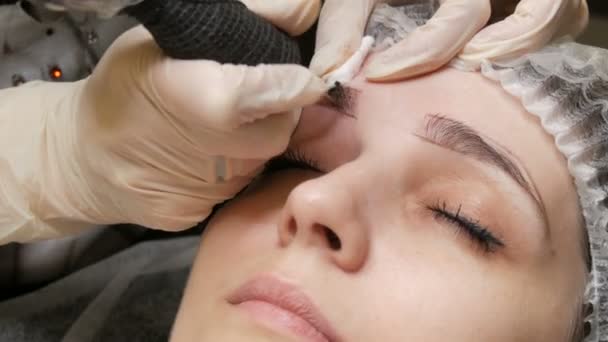 Özel bir iğne dövme makinesi genç bir kadının kaşlarını kalıcı olarak düzeltir. Derinin altına koyu boya pigmenti enjekte edilir. Mikro patinaj, barut püskürtme — Stok video